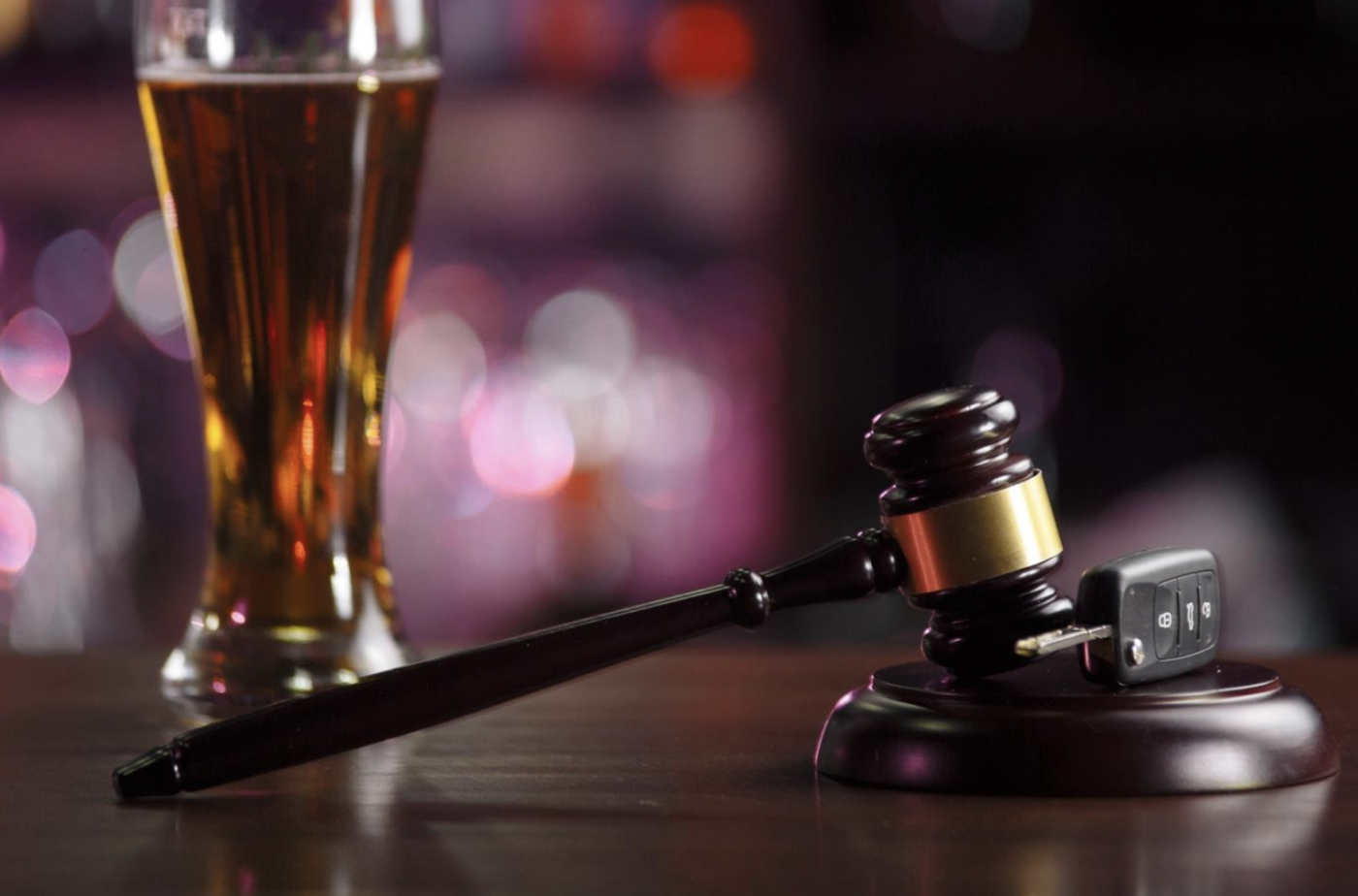 A wooden gavel beside a car key on a bar with a glass of beer in the background, symbolizing the potential impact of DUI charges on professional licensing and legal responsibilities.