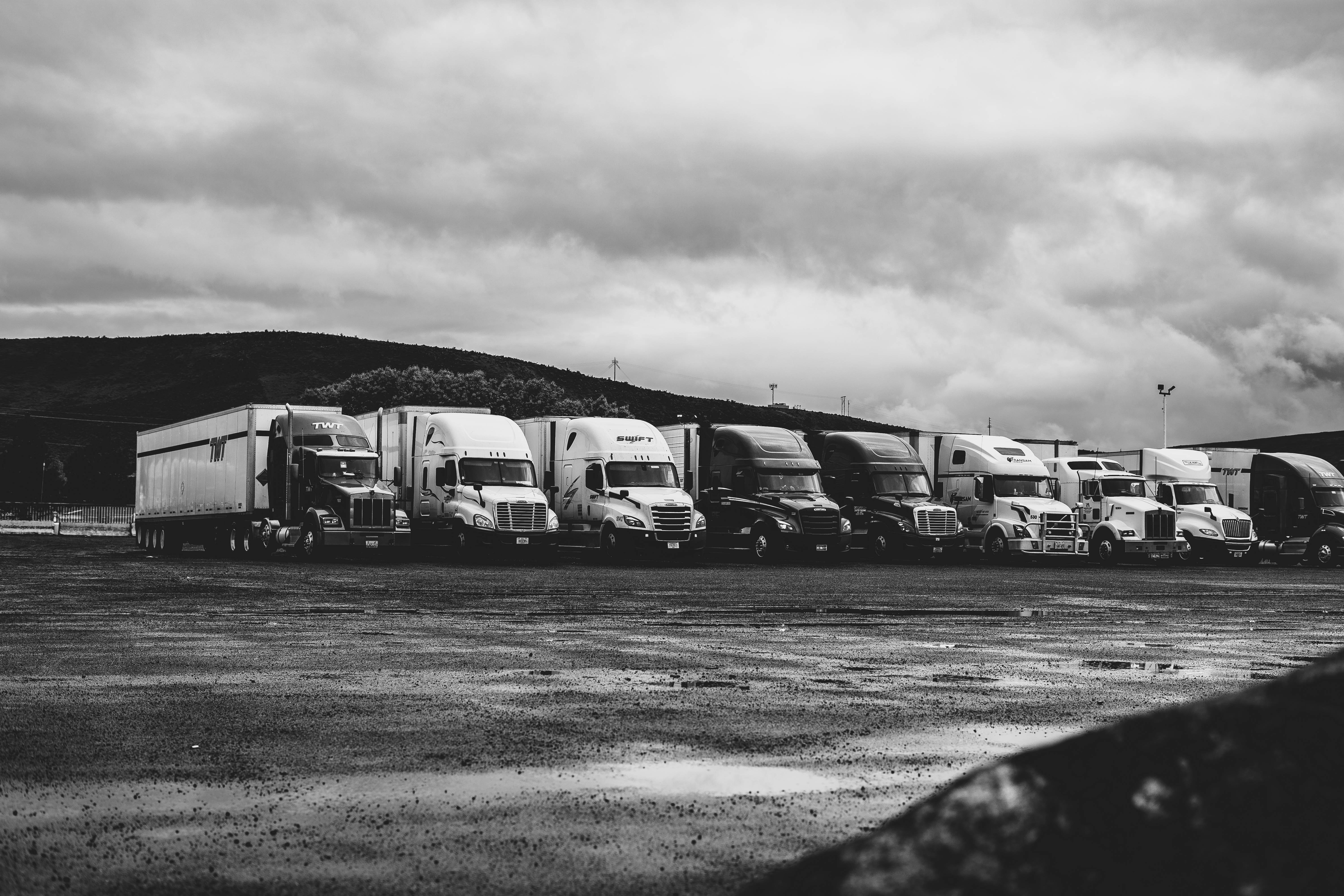 Black and white image showing a row of parked semi-trucks in a lot, with cloudy skies above, depicting commercial trucking vehicles which could be involved in specialized transportation accidents, associated with a blog post discussing the unique aspects of trucking accidents compared to other car accidents.