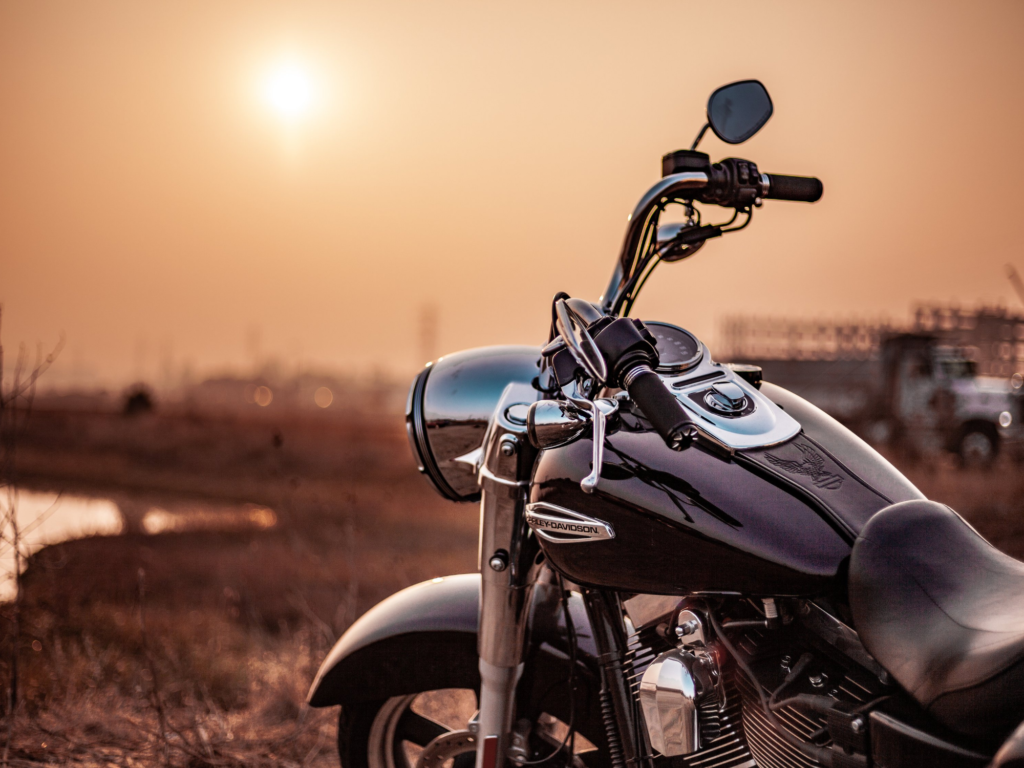 A parked motorcycle with a clear focus on its shiny chrome details, set against a blurred background of a sunset, evoking a sense of calm before the potential dangers leading to common motorcycle injuries from accidents.