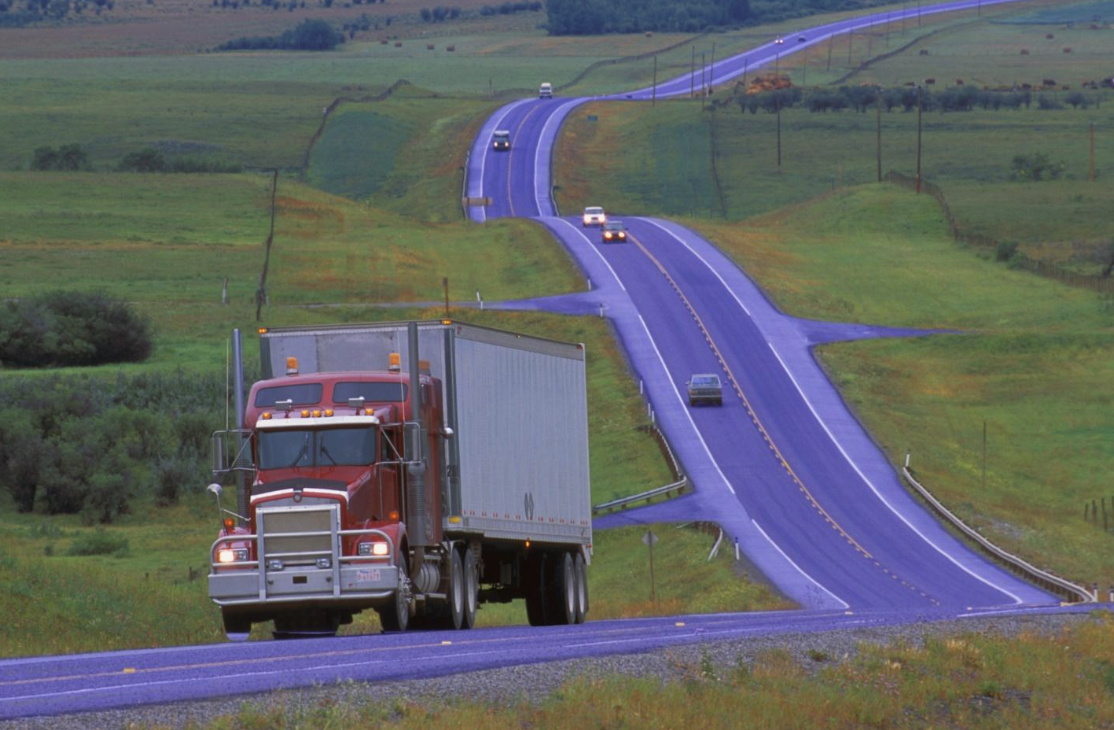 A large red truck parked on the side of a curving highway with other vehicles in motion, highlighting the hazards of parked trucks on busy roads.