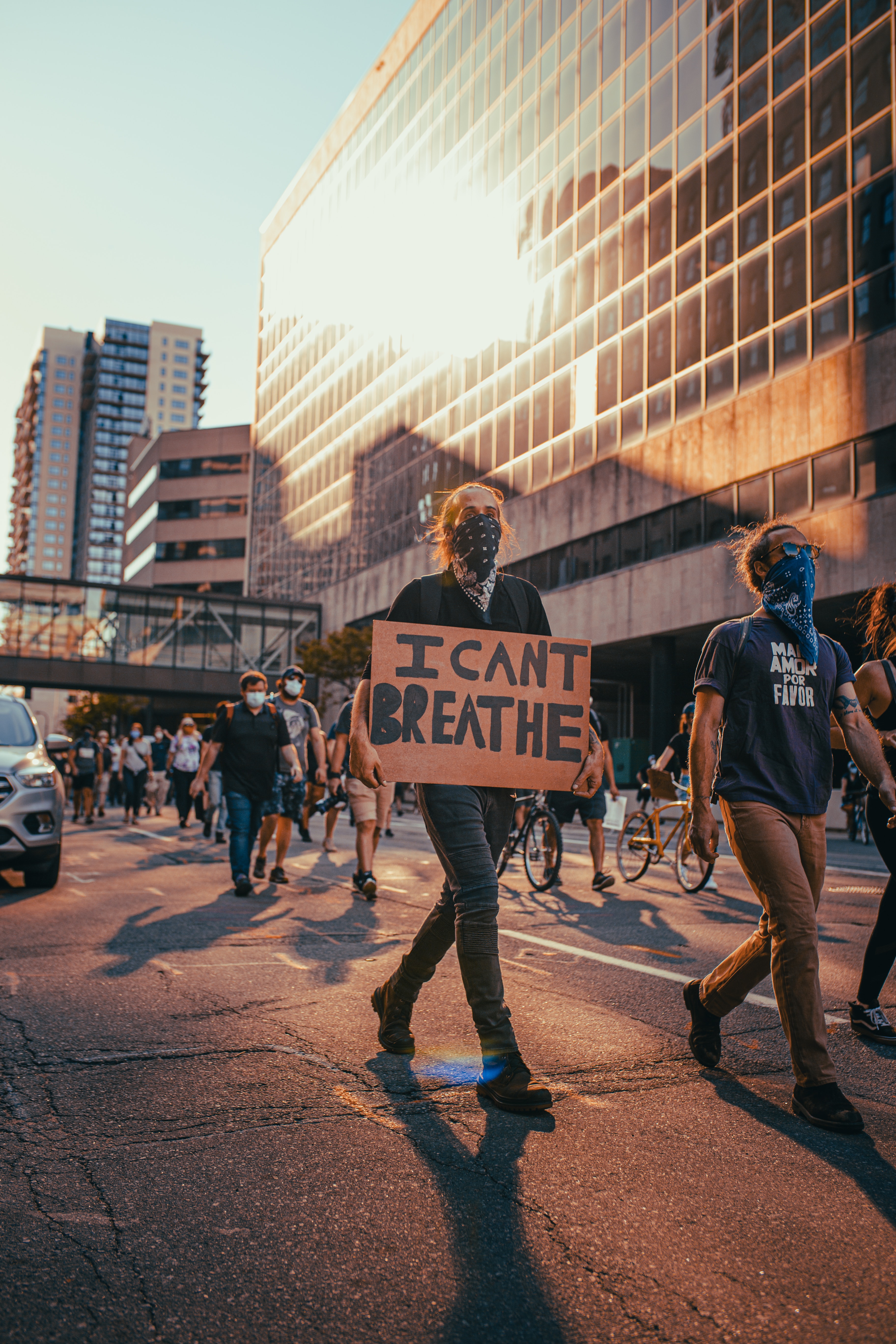 A protestor holding a sign that reads 'I CAN'T BREATHE' during a demonstration, with others around on a city street at sunset, reflecting the sentiments of the Black Lives Matter movement.