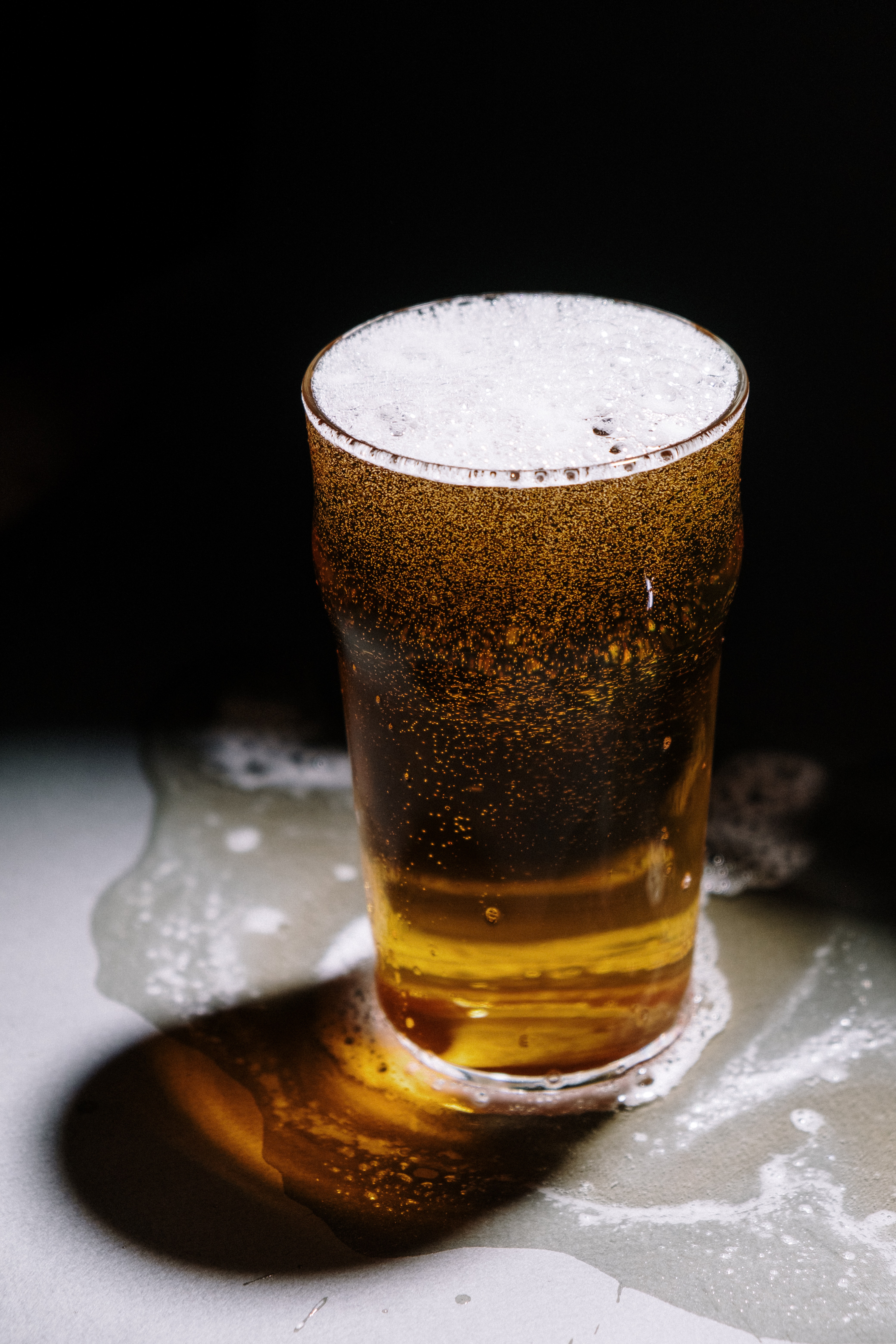 A pint glass of beer with overflowing foam on a table, creating a spill, indicative of potential overconsumption, relevant to discussions on the legal implications of a first offense DUI in Arizona.