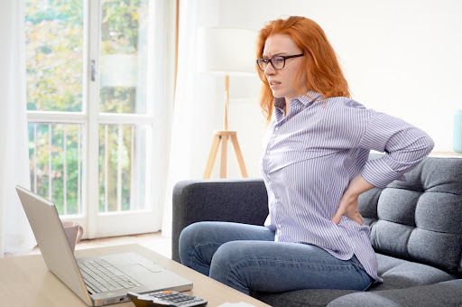 Woman in casual attire experiencing back pain while working on a laptop at home, representing the potential long-term effects of car accidents on personal health and daily activities.