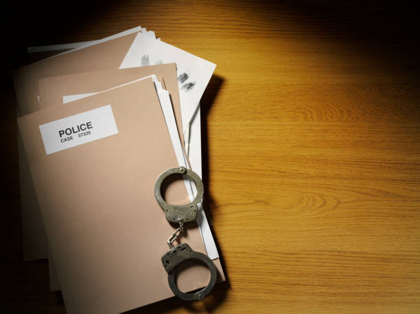 Police case file folders and handcuffs on a wooden surface, symbolizing the legal implications of manipulating police reports.