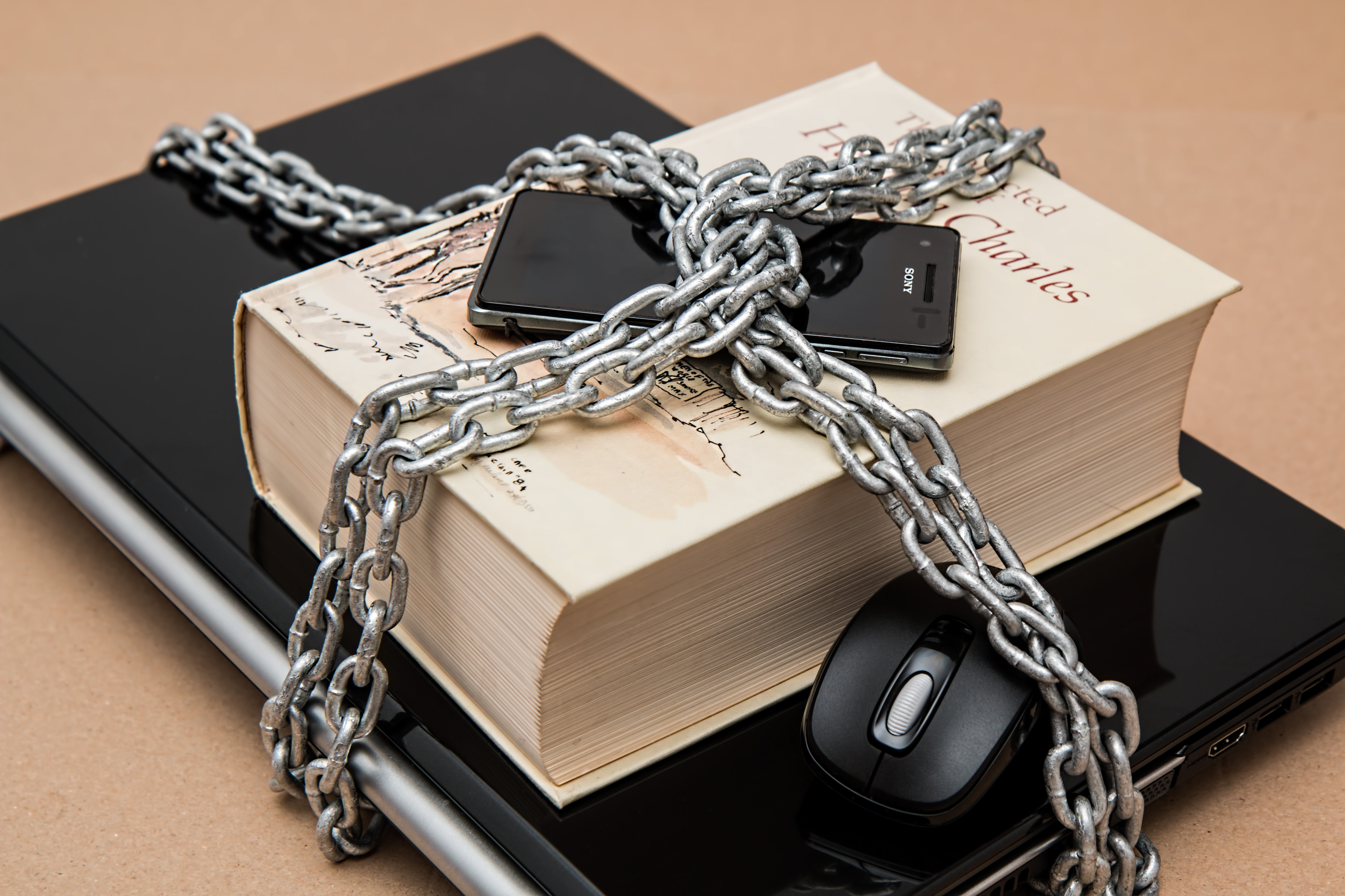 A book titled 'The End of Privacy' and electronic devices including a smartphone and a laptop wrapped in heavy metal chains, symbolizing the protection of personal privacy and the concept of 'Our privacy is not for sale'.