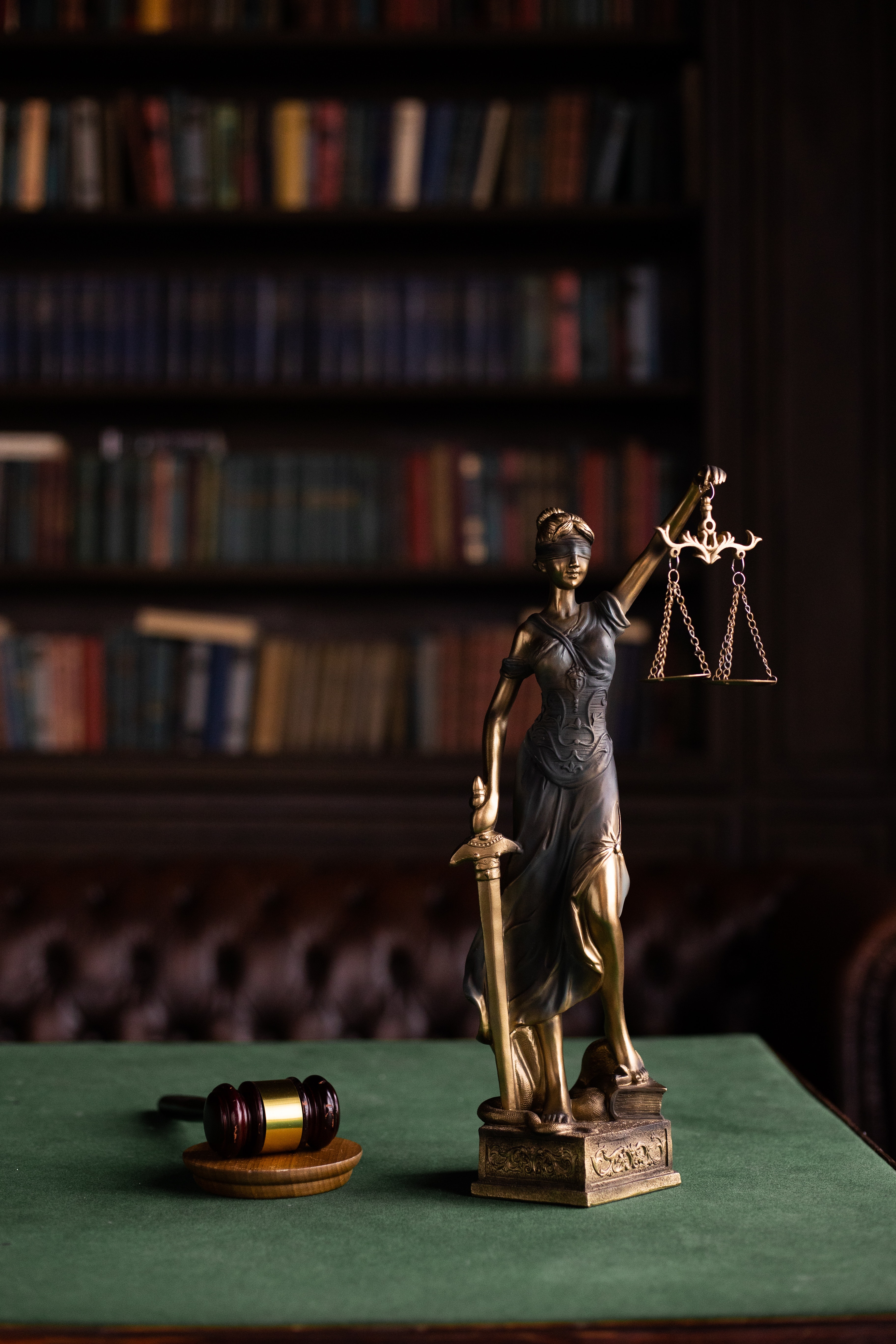 Bronze statue of Lady Justice holding scales and sword, with a gavel in the foreground, against a backdrop of a law library, relating to potential 2021 changes to Arizona criminal laws.