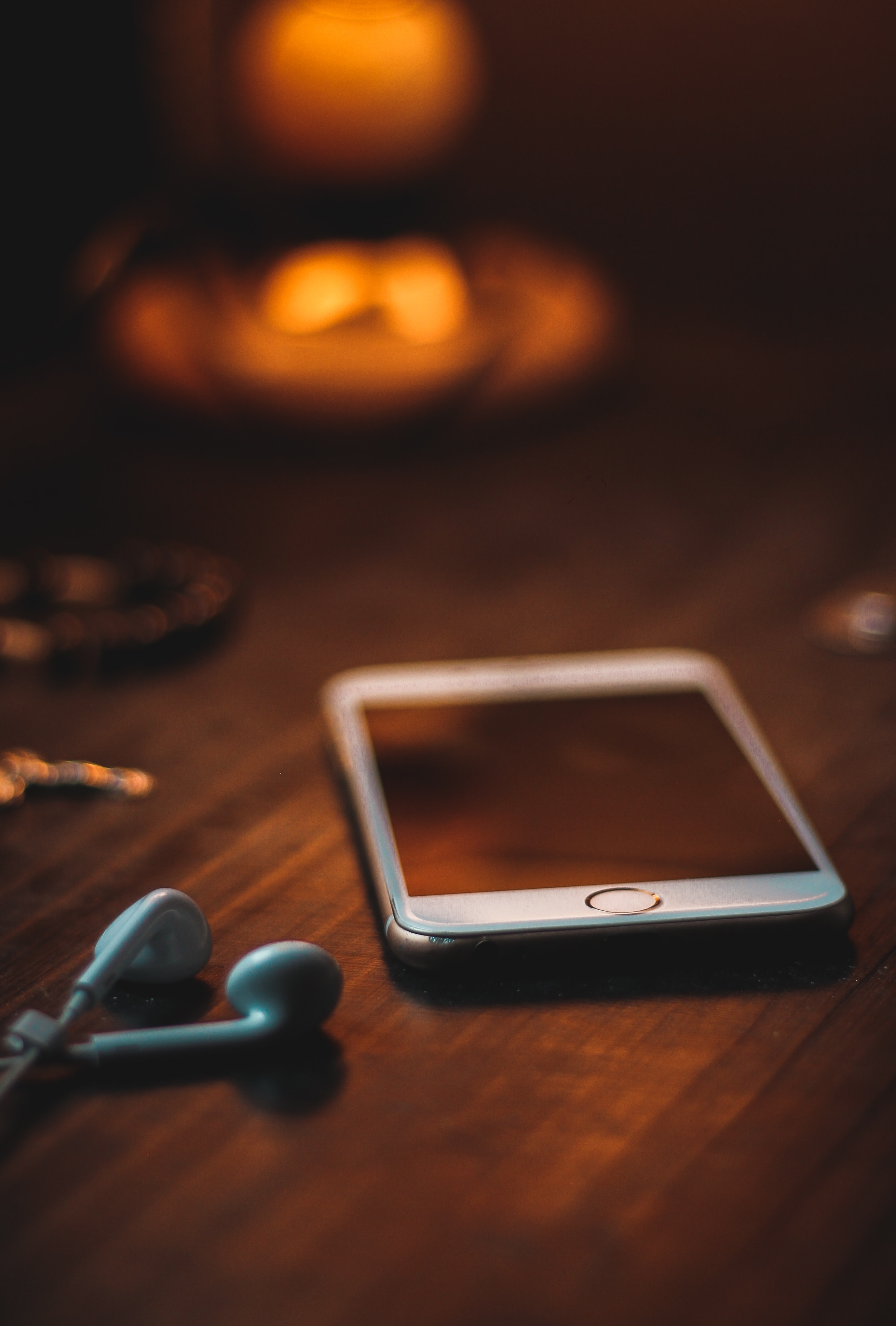 Smartphone with earphones on a wooden surface with a soft-focus candle in the background, suggesting a personal ambiance possibly related to a legal discussion about cellphone search warrants.