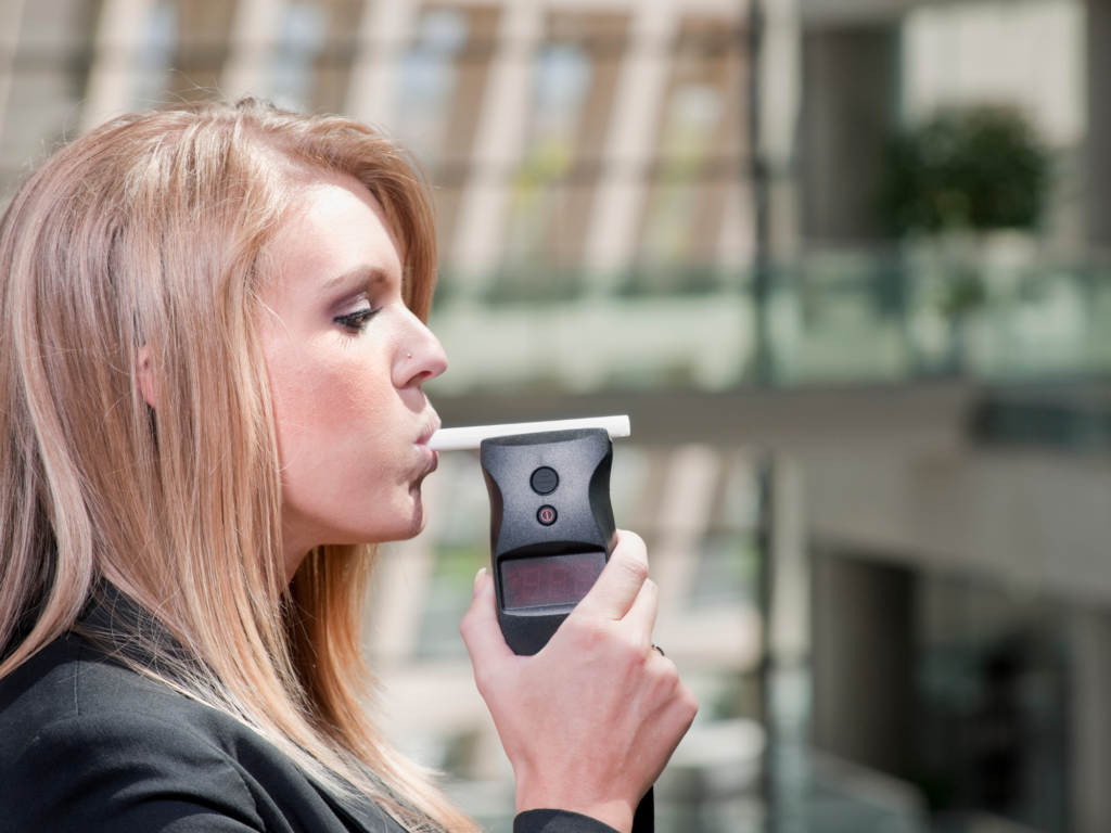 Woman performing a breathalyzer test outdoors, with the device in focus, pertinent to legal advice on whether to submit to such a test in Arizona.