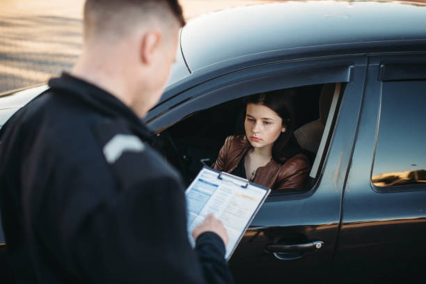 Police officer reviewing a document during a traffic stop with a female driver looking on from inside her vehicle, reflecting a common roadside law enforcement scenario.