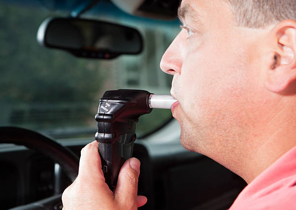 Man using a car breathalyzer interlock device before starting vehicle, ensuring compliance with DUI laws.